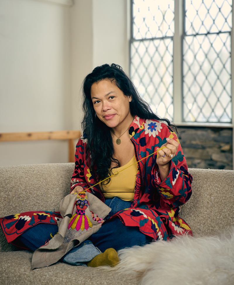 Artist Christi Johnson sitting on a couch embroidering